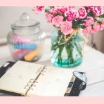 Desk planner, roses, and jar with colored chalk on an office desk at home